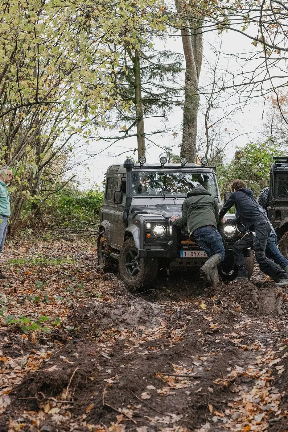 Deelnemers duwen samen een Defender uit de modder