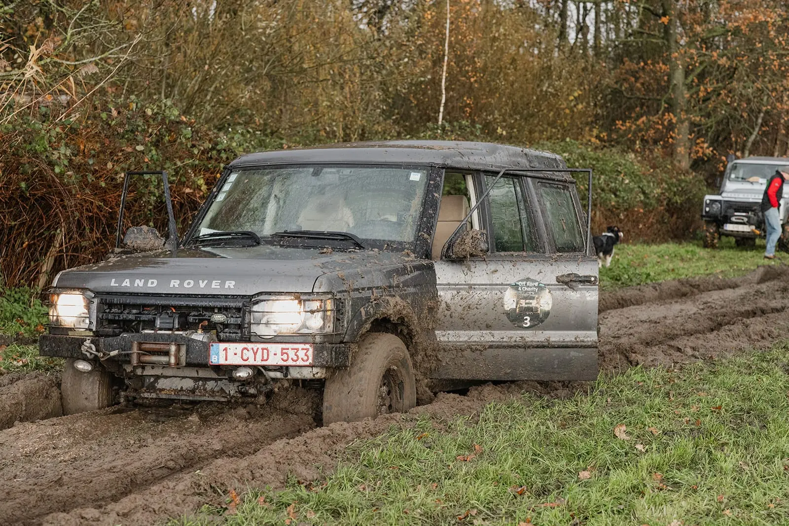 Een Land Rover Discovery vol modder rijdt door een diepe bosweg